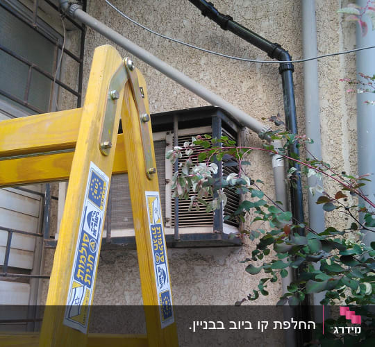 סולם צהוב ליד צינורות שחורים על קיר חיצוני